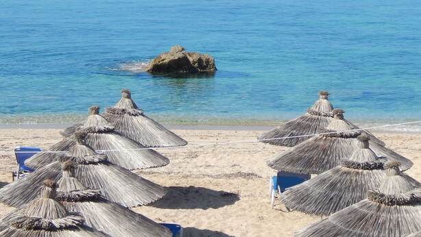 Una playa con sombrillas de paja y una vista despejada del mar.