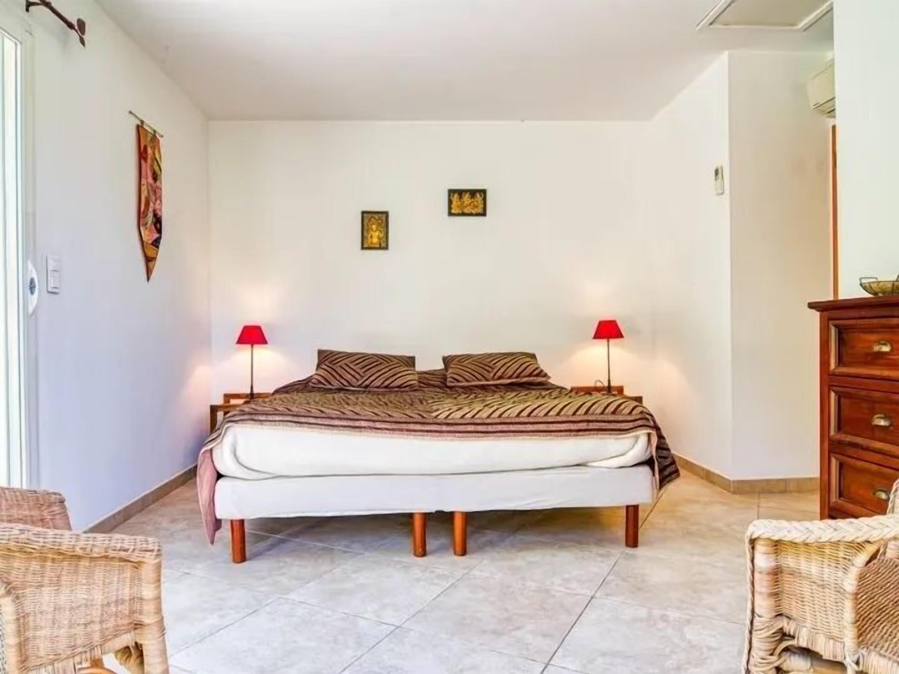 A bedroom with a bed, two wall-mounted lamps, a wooden dresser, and a wicker chair.