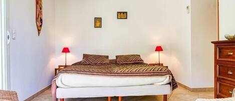 A bedroom with a bed, two wall-mounted lamps, a wooden dresser, and a wicker chair.