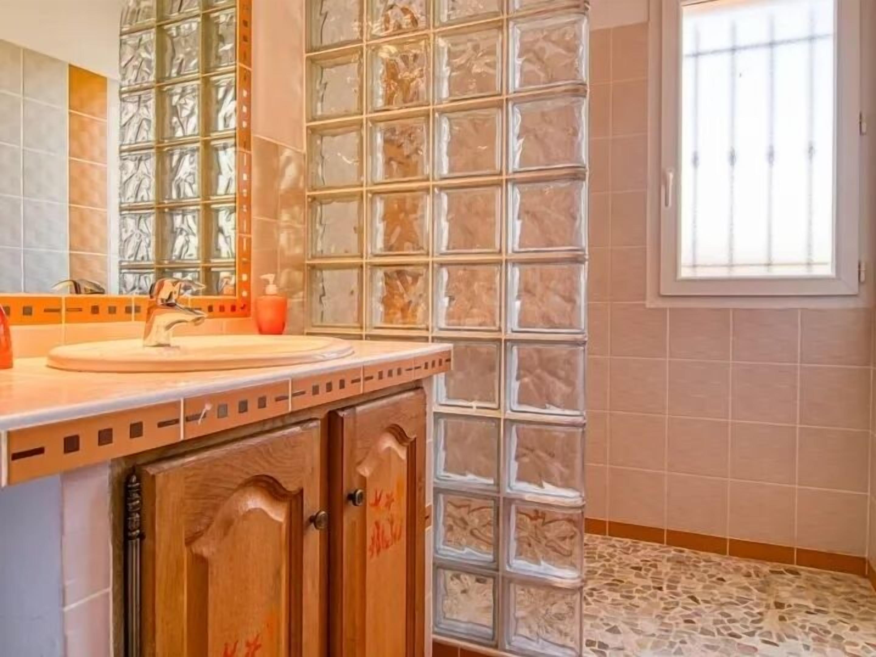 A bathroom with a glass block wall, a sink with a mirror, and a window.