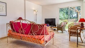 A room with a metal-framed sofa with red cushions, a television, wicker chairs, and a view of greenery through large windows. - Recent Provencal villa, 8 rooms, all comfort with swimming pool on closed space (Cotignac, Monfort sur Argens)