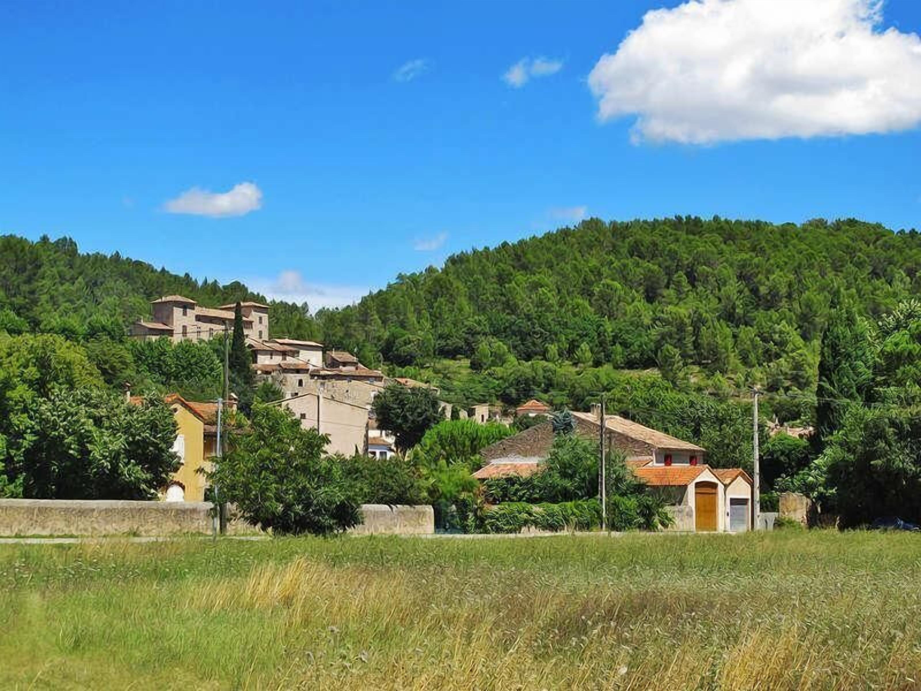 A hillside village with traditional buildings, a clear sky, and lush greenery.