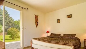 A bedroom with a bed, a chair, a red lamp, and a view of greenery outside. - Recent Provencal villa, 8 rooms, all comfort with swimming pool on closed space (Cotignac, Monfort sur Argens)
