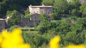 A stone building with multiple windows, surrounded by lush greenery and hills in the background. - Gîte de Chapelèche "Les Genêts" (Gluiras)