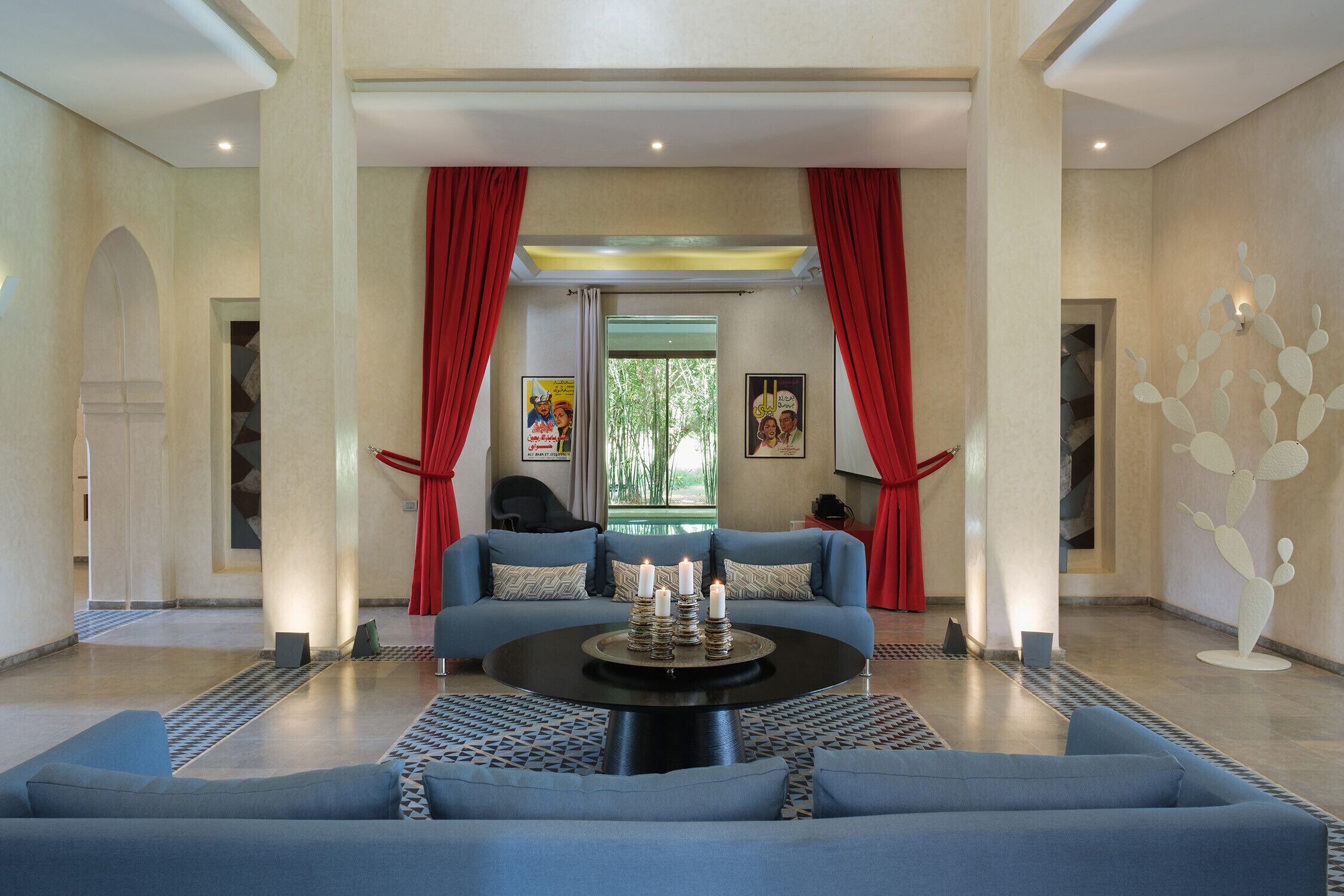 A spacious lobby with a blue sofa, a round coffee table with candles, red curtains, and a modern wall art piece.