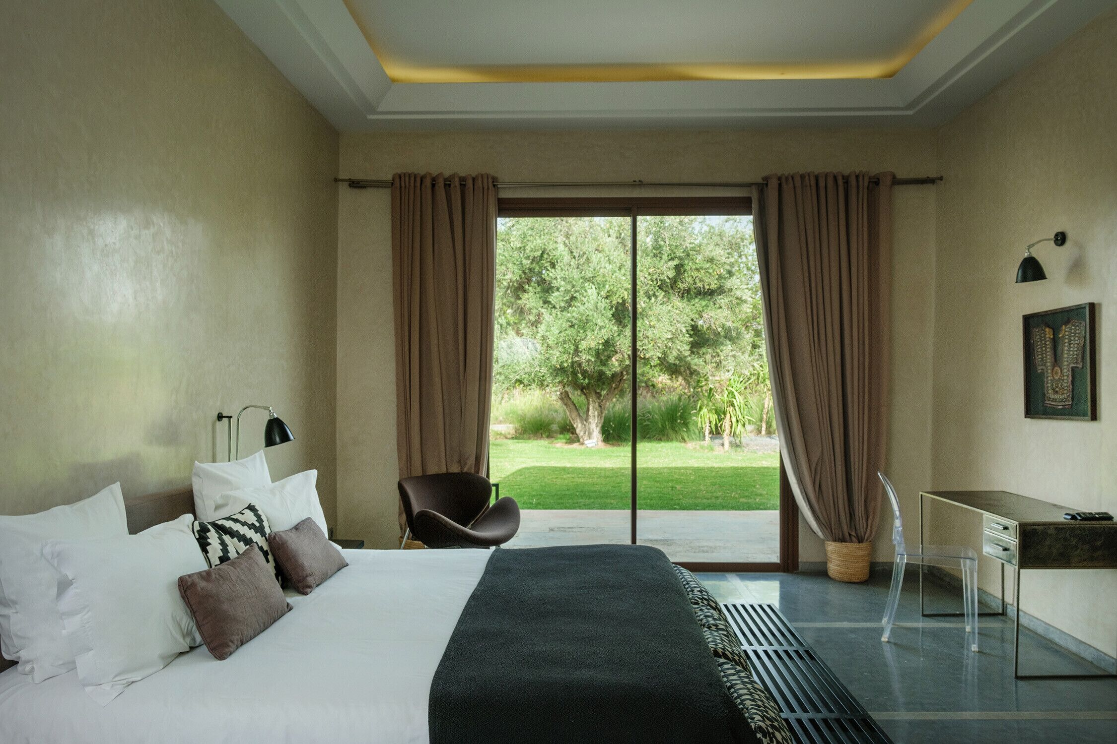 Habitación de hotel con cama, escritorio, silla y vista a un jardín a través de una puerta corrediza.