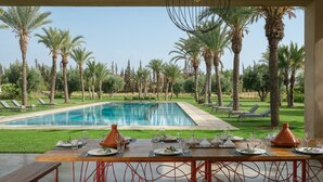 A dining area with a pool view, outdoor seating, and palm trees. - ADNAA - Luxury Villa with 2 pools, sauna, hammam, tennis court & home cinema (Marrakech)