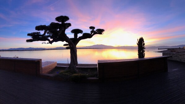 A sunset view over a calm lake with a wooden deck and seating areas.