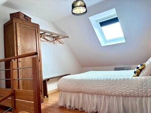 A bedroom with a sloped ceiling, a skylight, a wooden wardrobe, a bed with white bedding, and a hanging light fixture.