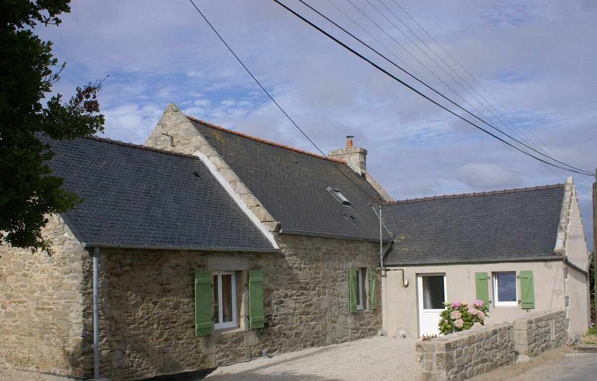 Un bâtiment en pierre avec un toit en pente et des volets verts.