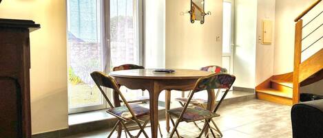 Un comedor con una mesa redonda y cuatro sillas, una ventana con cortinas, un espejo en la pared y una escalera.