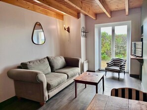 A living room with a sofa, a coffee table, a TV, and a view of greenery outside.