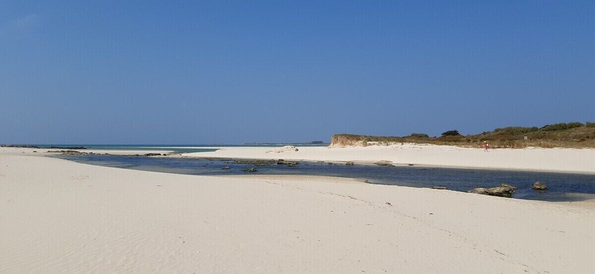Une vaste plage de sable fin, avec un ciel dégagé et une mer calme.