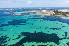 An aerial view of a coastal area with clear turquoise waters, rocky outcrops, and a distant shoreline with buildings. - Reder Mor : maison de pêcheurs 250 m de la mer (SANTEC)