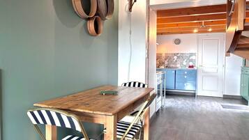 Un coin repas avec une table en bois et des chaises à rayures, une cuisine en arrière-plan et un escalier avec des poutres en bois.