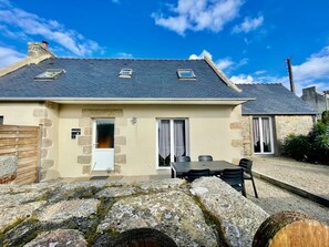 A stone house with a tiled roof, a small patio with a table and chairs, and a stone wall in the foreground. - Reder Mor : maison de pêcheurs 250 m de la mer (SANTEC)