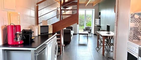 A modern kitchen with a built-in washing machine, a red coffee maker, and a microwave. There is a staircase leading to an upper level.