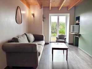 A modern living room with a grey sofa, a striped armchair, a small table, and a TV on a shelf. - Reder Mor : maison de pêcheurs 250 m de la mer (SANTEC)