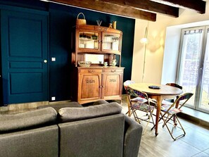 A cozy living room with a dark blue door, a wooden cabinet with glass doors, a round wooden table, and a gray sofa. - Reder Mor : maison de pêcheurs 250 m de la mer (SANTEC)