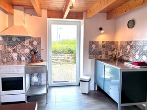 A modern kitchen with patterned tiles, a stove, a sink, and a window leading to an outdoor area. - Reder Mor : maison de pêcheurs 250 m de la mer (SANTEC)