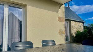 An outdoor patio with a table and chairs, a stone wall, and a building with a sloped roof. - Reder Mor : maison de pêcheurs 250 m de la mer (SANTEC)