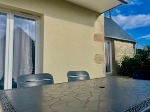 An outdoor patio with a table and chairs, a stone wall, and a building with a sloped roof. - Reder Mor : maison de pêcheurs 250 m de la mer (SANTEC)