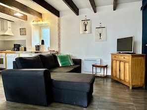 A modern living room with a sofa, a television on a wooden cabinet, and a kitchen area with a dishwasher and a coffee maker. - Reder Mor : maison de pêcheurs 250 m de la mer (SANTEC)