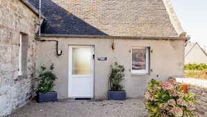 A small stone building with a white door, two windows, and a gravel driveway.