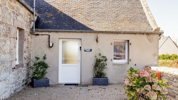 Un petit bâtiment en pierre avec une porte blanche, deux fenêtres et une allée gravillonnée.