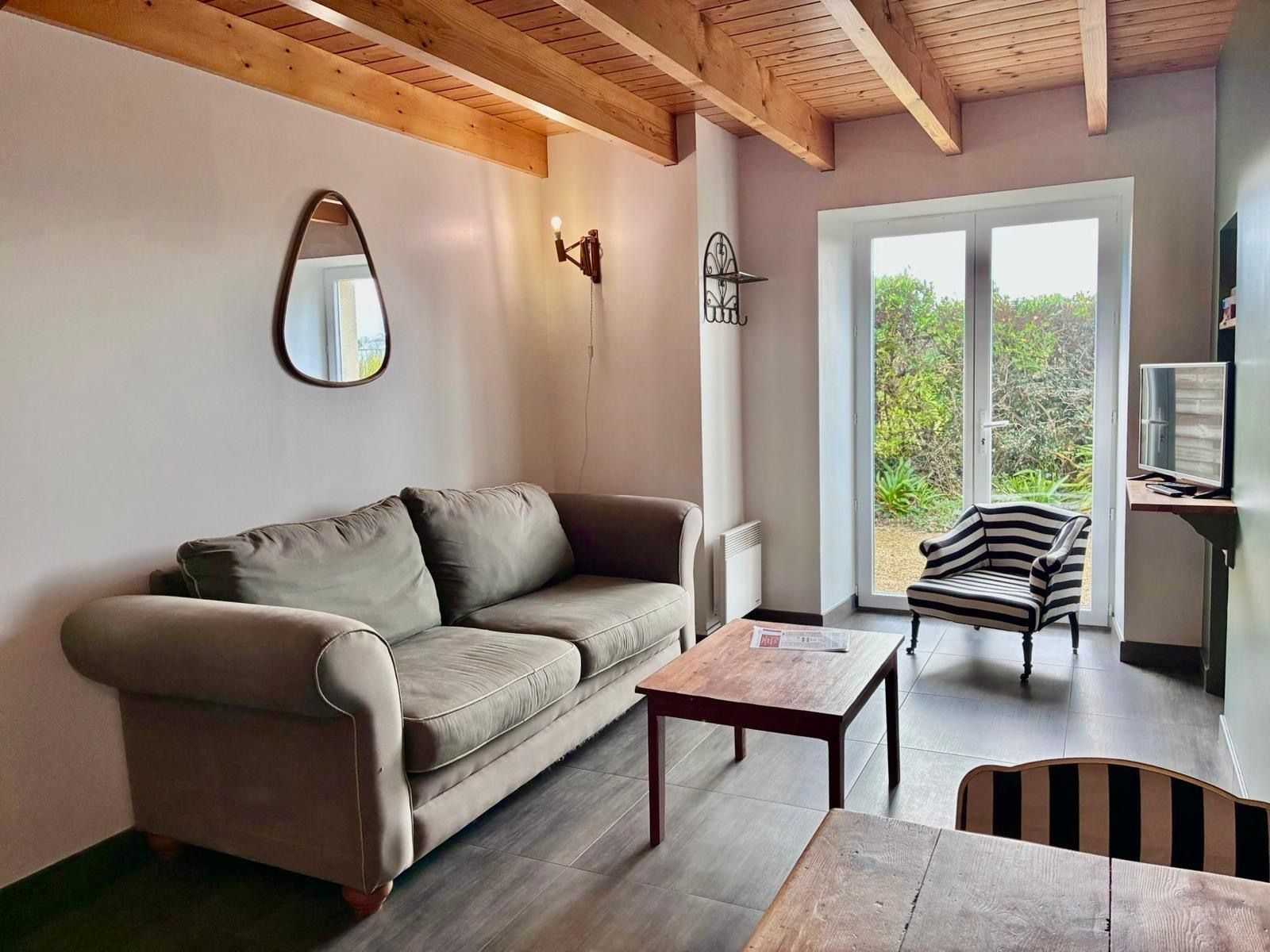 A living room with a sofa, a coffee table, a TV, and a view of greenery outside.