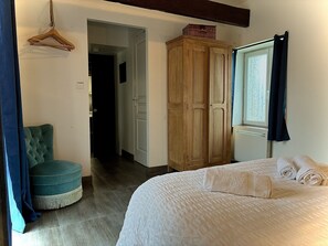 A bedroom with a bed, a wooden wardrobe, a hanging wardrobe, a blue chair, and a window with curtains. - Reder Mor : maison de pêcheurs 250 m de la mer (SANTEC)