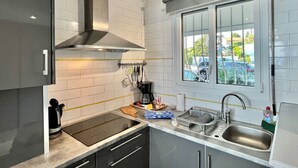 Une cuisine moderne dotée d’une cuisinière intégrée, d’une hotte en acier inoxydable, d’une fenêtre donnant sur les voitures garées et d’un évier avec un égouttoir.