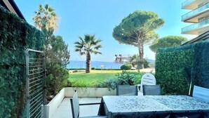 Une terrasse extérieure avec une table et des chaises, donnant sur un espace verdoyant avec des arbres et offrant une vue sur la mer.