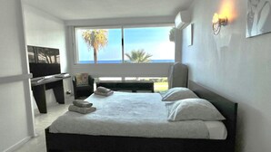 Une chambre à coucher comprenant un lit, un bureau, une chaise et une grande fenêtre donnant sur la mer.