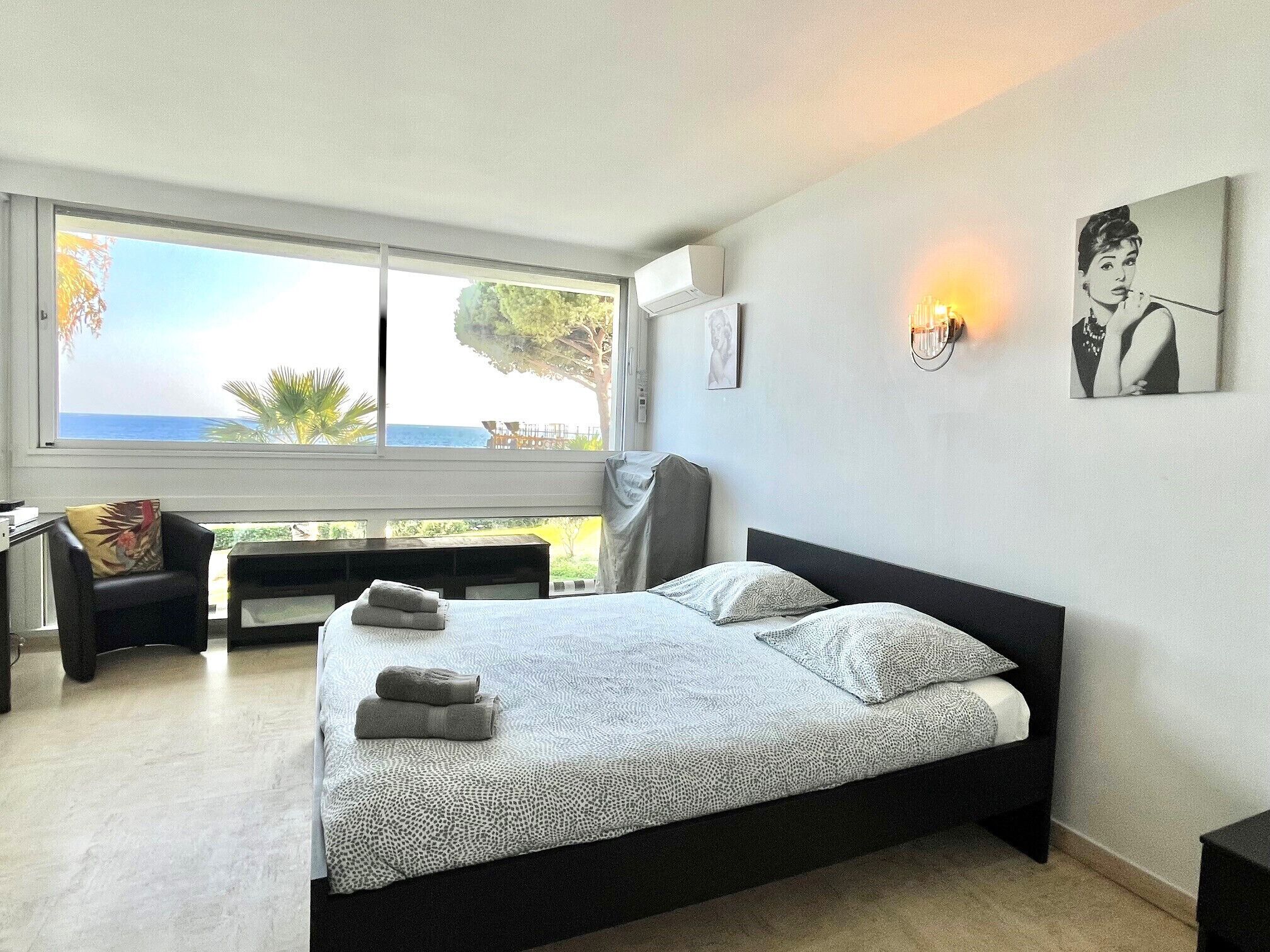 Een slaapkamer met een groot bed, een bureau en een stoel. Er is een raam met uitzicht op de oceaan.