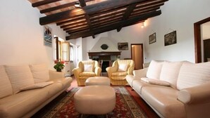 Ein Wohnzimmer mit hohen Decken, Holzbalken, zwei Sofas, zwei Sesseln, einem Teppich und einem Kamin.