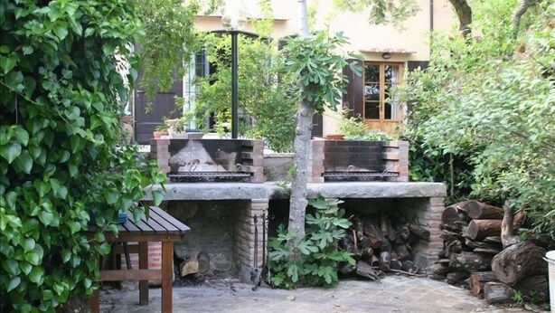 Ein Terrassenbereich im Freien mit Kamin aus Stein, einem Holztisch und einem Holzstapel.