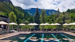 A pool area with lounge chairs and umbrellas, surrounded by trees and mountains.