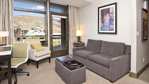 Habitación de hotel con sofá, sillón, mesa de centro y vista a un paisaje montañoso a través de un ventanal grande.
