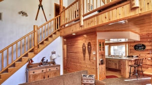 A wooden interior with a staircase, a sofa with patterned cushions, a kitchen area, and a sign that reads "Pine Lodge". - Pine Lodge at Snow Summit.  Spa and Pool Table! (Big Bear)