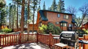 A wooden cabin with a deck, a barbecue grill, and a view of surrounding trees. - Pine Lodge at Snow Summit.  Spa and Pool Table! (Big Bear)