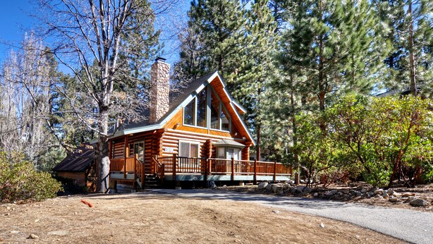 A log cabin with a prominent chimney, surrounded by dense forest. - Pine Lodge at Snow Summit.  Spa and Pool Table! (Big Bear)