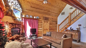 A cozy log cabin interior with a stone fireplace, wooden furniture, and a staircase. - Pine Lodge at Snow Summit.  Spa and Pool Table! (Big Bear)