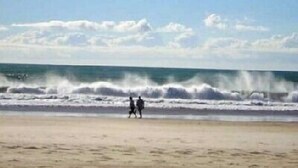 Una playa con olas rompiendo en la orilla y dos personas caminando por la orilla del agua.