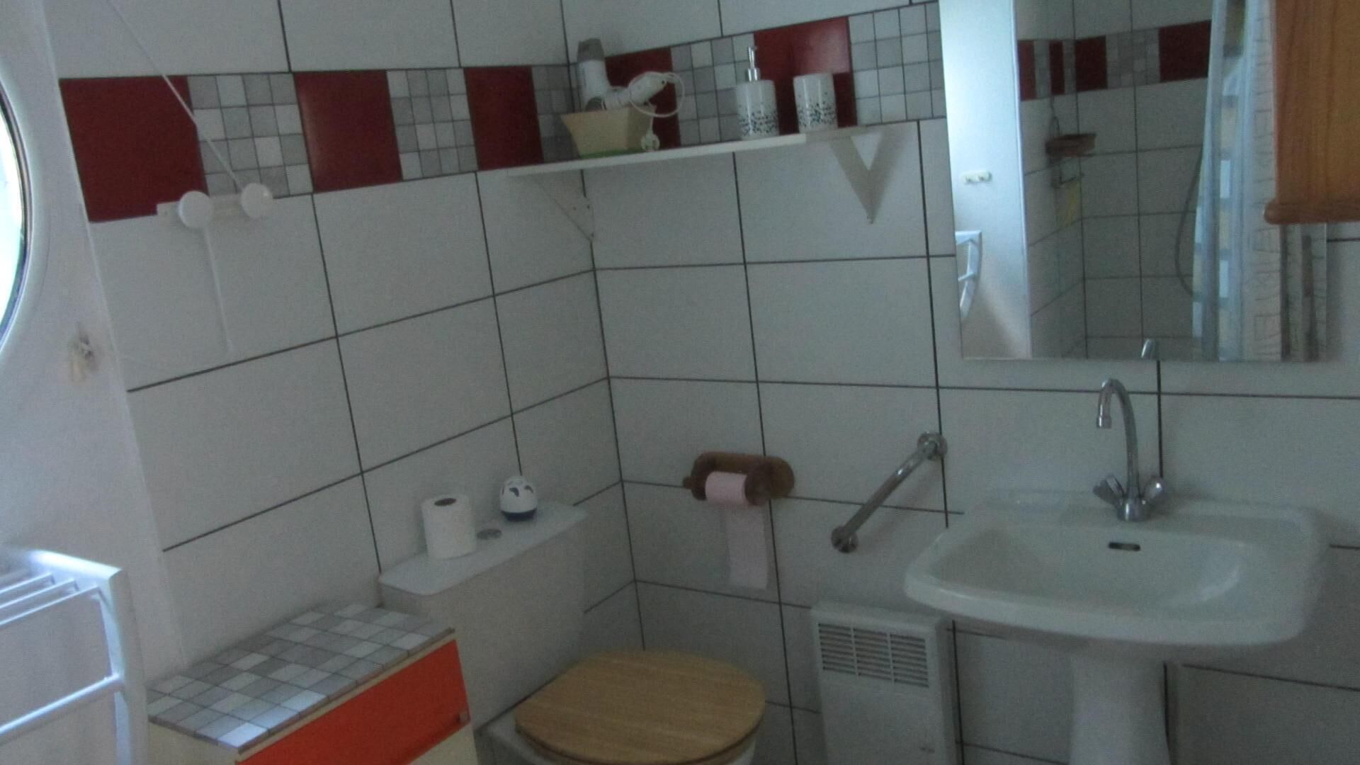 Un bagno piccolo con WC, lavandino e specchio. Sopra il WC c'è uno scaffale con articoli da toilette.