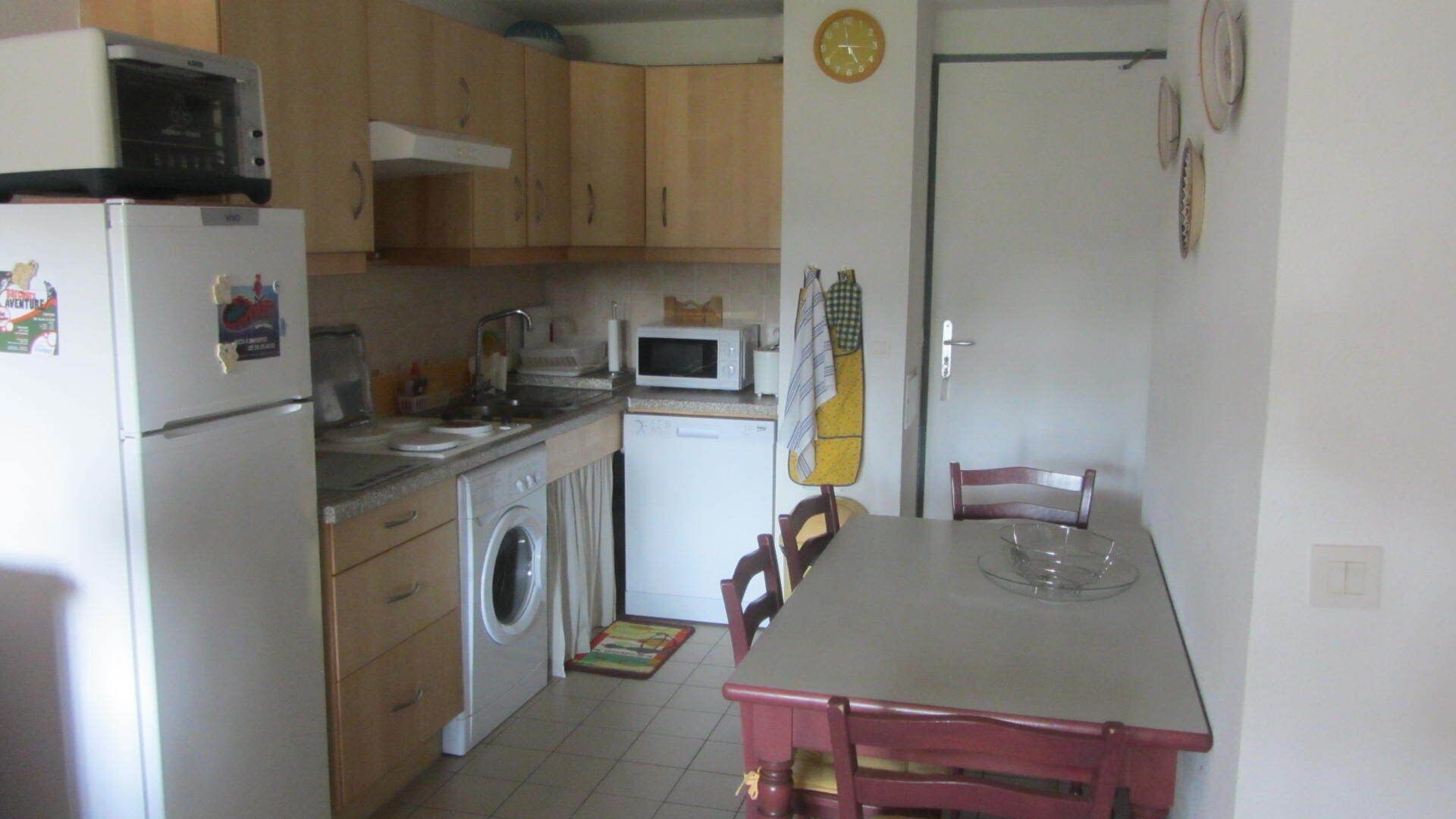 A compact kitchen with a refrigerator, microwave, washing machine, and a dining table with chairs.