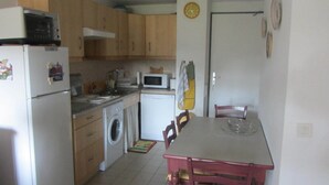Cocina compacta con refrigerador, microondas, lavadora y una mesa de comedor con sillas.
