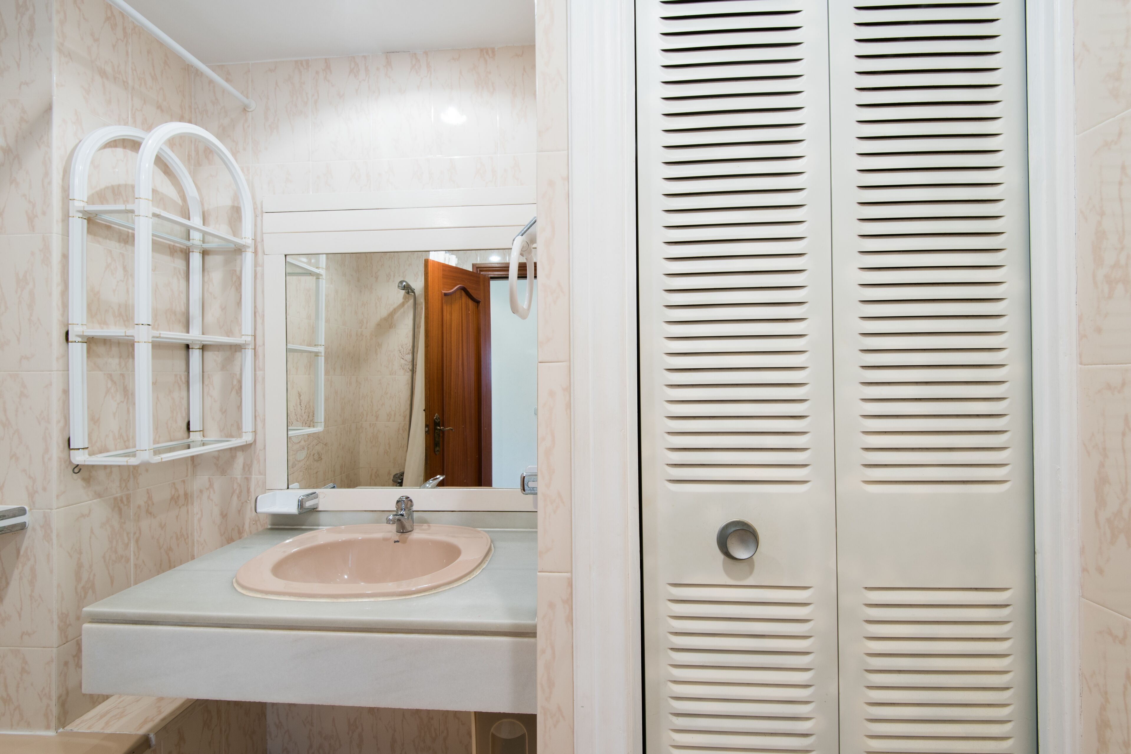 A bathroom with a sink, mirror, and a door with louvered panels.