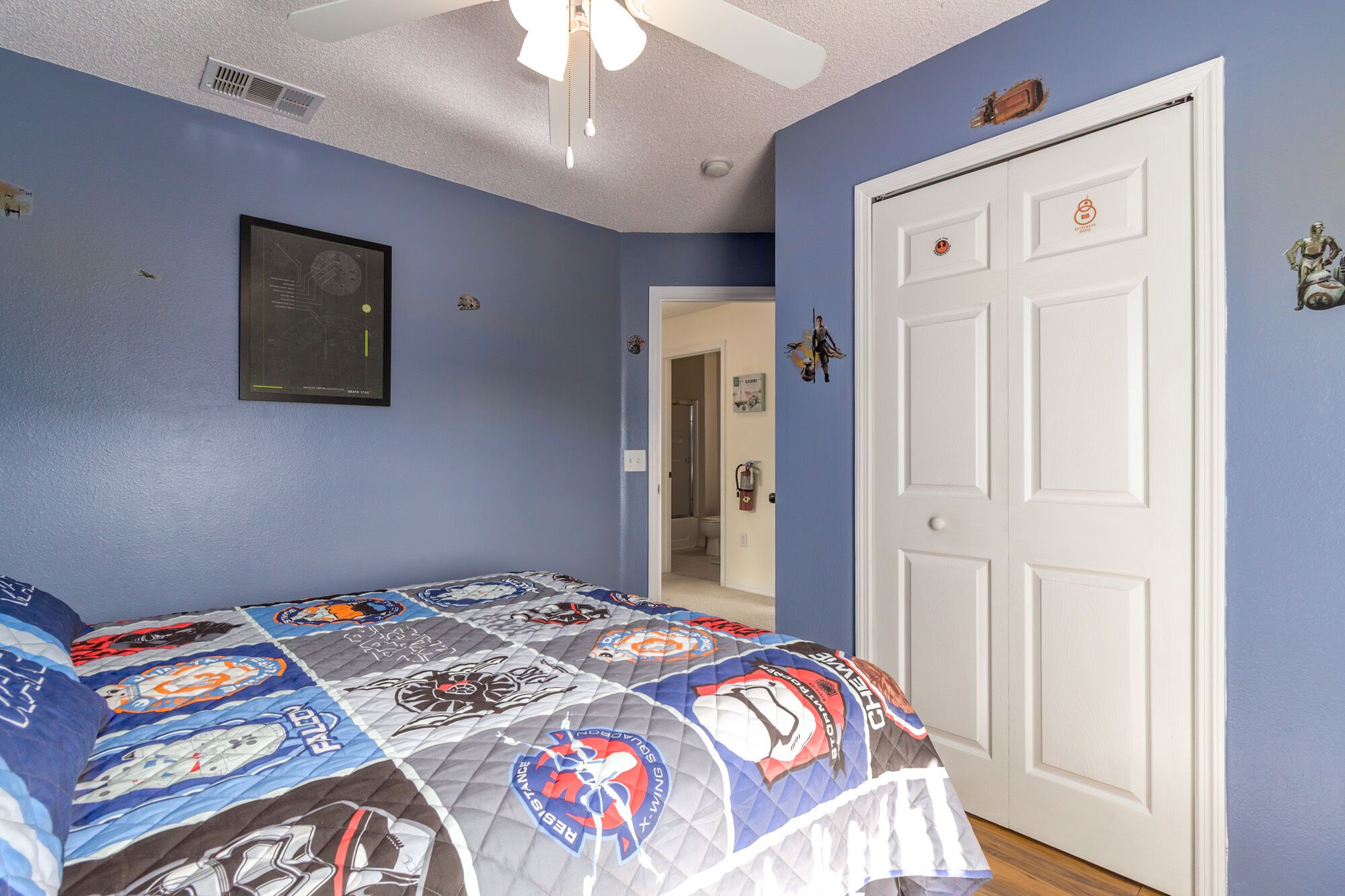 Un dormitorio con una pared azul, una puerta blanca y una cama con colcha temática de Star Wars.