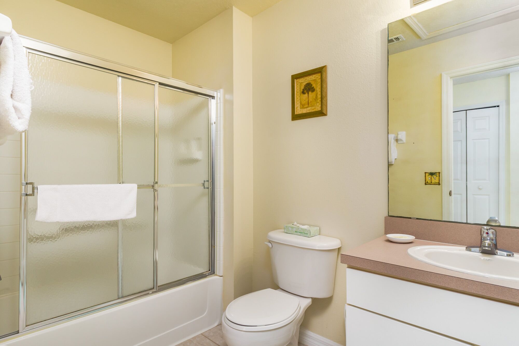 A bathroom with a glass-enclosed shower, a toilet, and a sink with a mirror above it.
